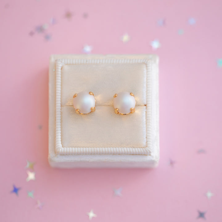 Pearl earrings with gold accents on a pink background