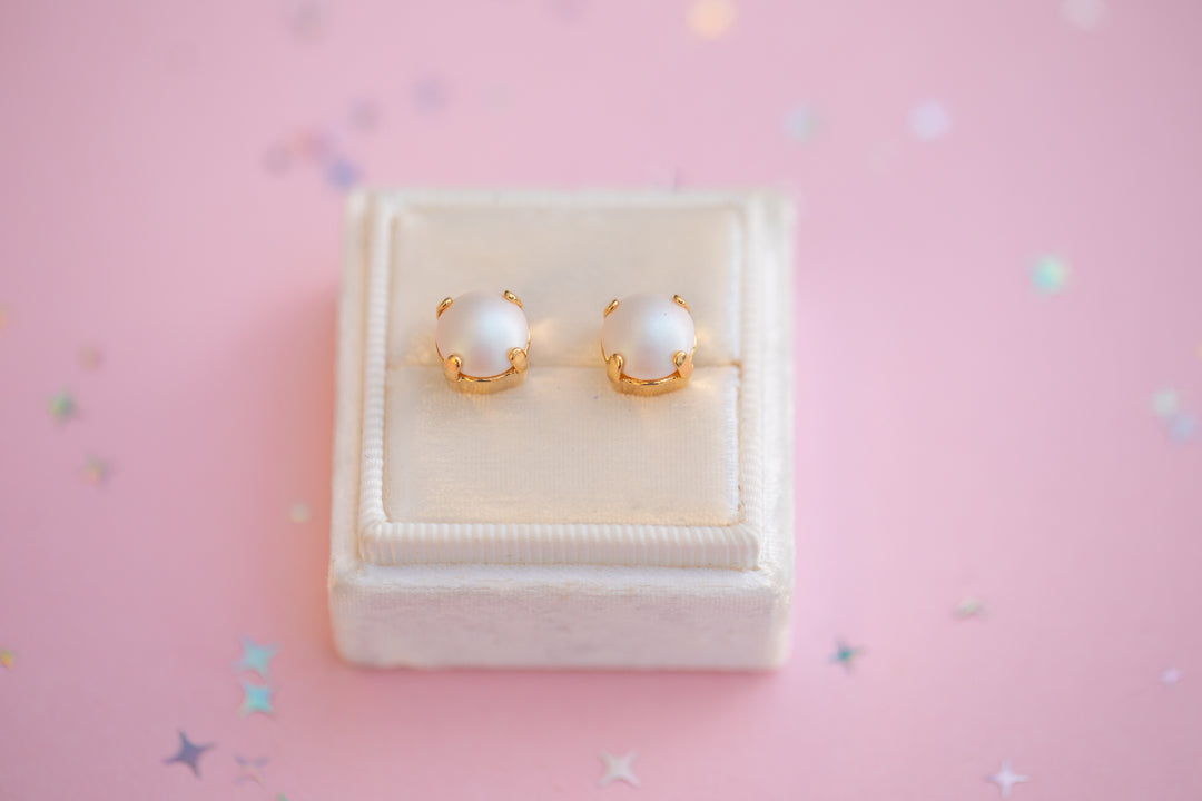 Pair of pearl earrings on a white jewelry box with a pink background