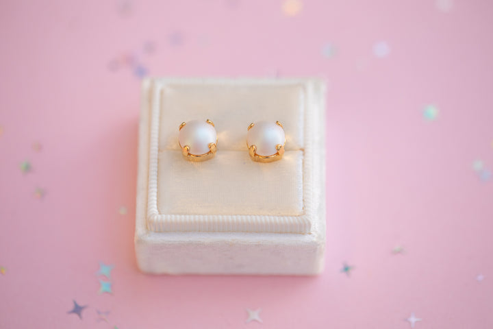 Pair of pearl earrings on a white jewelry box with a pink background