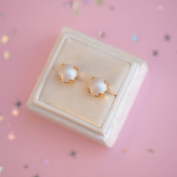 Pearl earrings with gold accents on a pink background