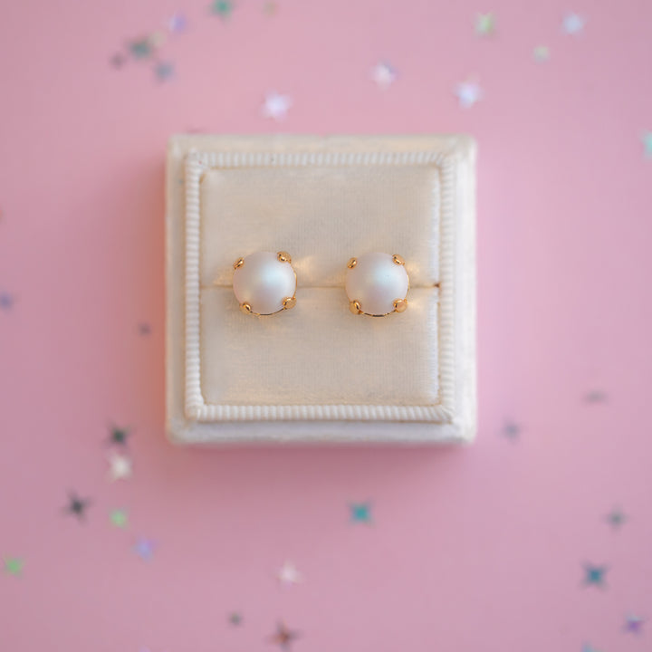 Pair of pearl earrings in a white box on a pink background with star-shaped decorations.