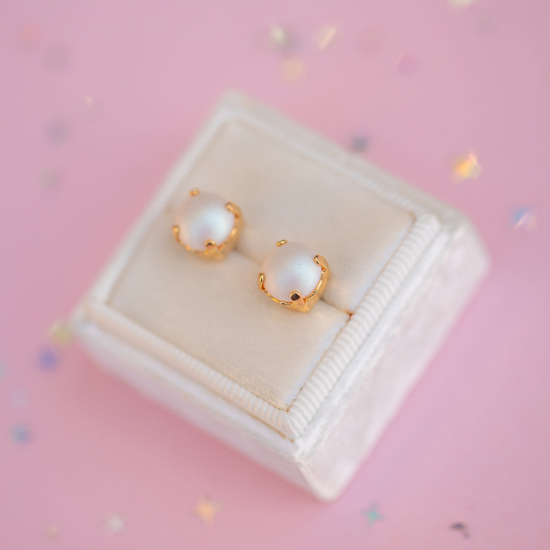 Pair of pearl earrings with gold accents on a pink background