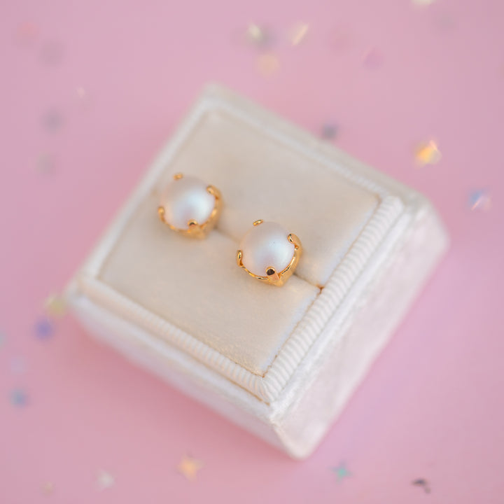 Pair of pearl earrings with gold accents on a pink background