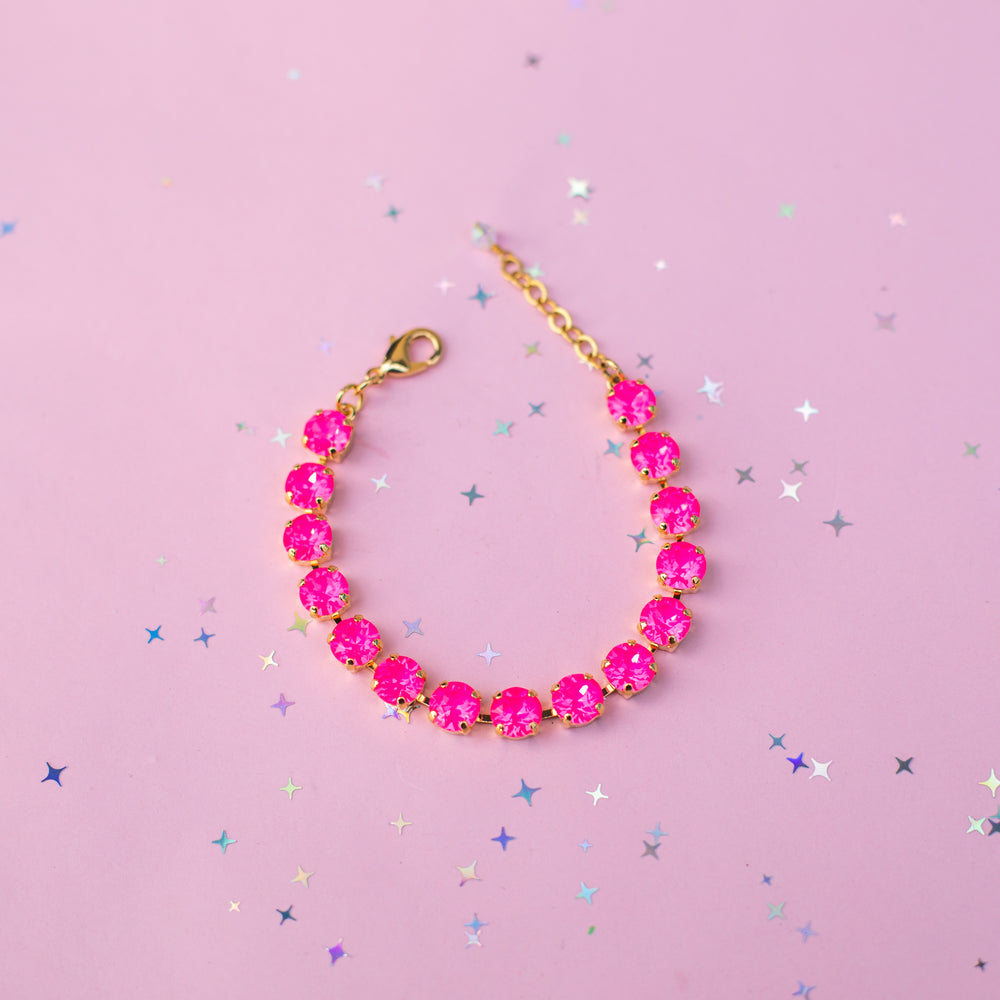 A gold chain bracelet with round, bright pink gemstones, displayed on a pink background with scattered silver star confetti.