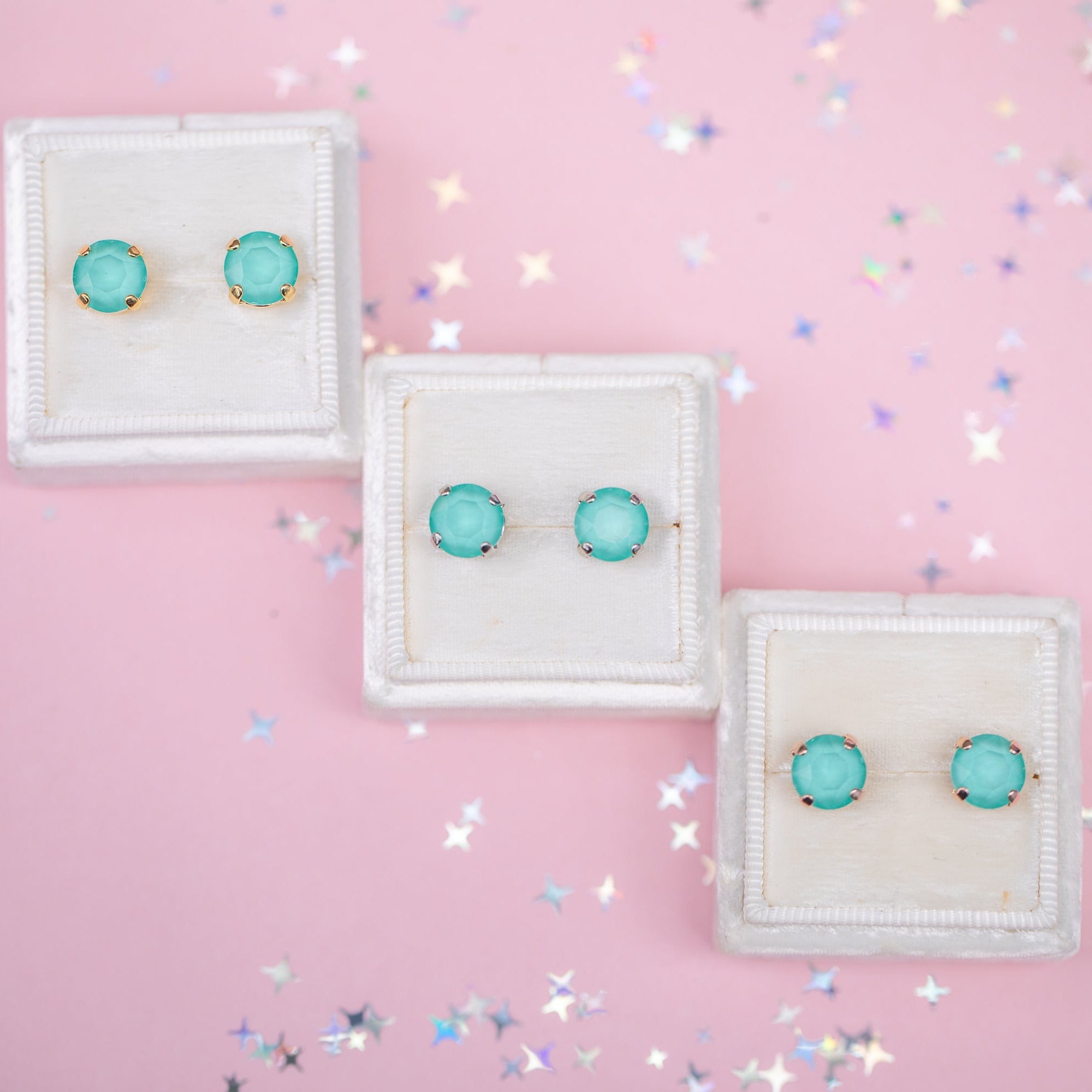 Turquoise earrings on white display cards against a pink background with confetti