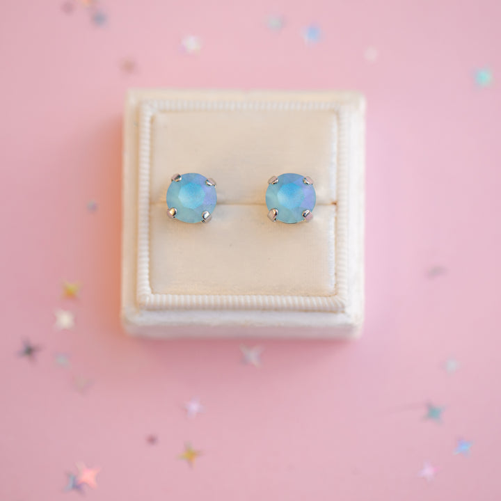 Opal stud earrings in a white box on a pink background