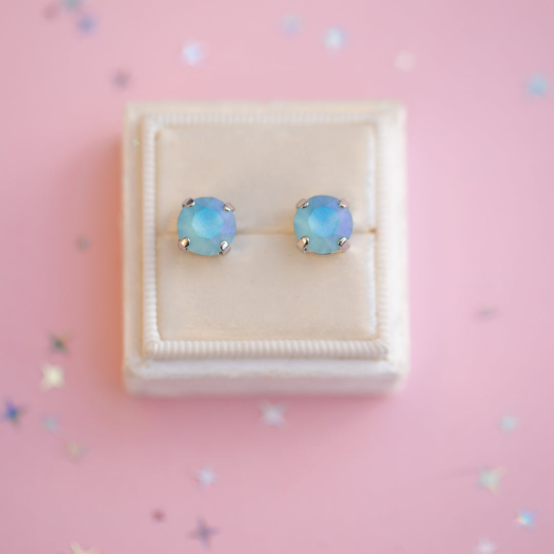 Pair of blue opal stud earrings in a white box on a pink background with confetti.