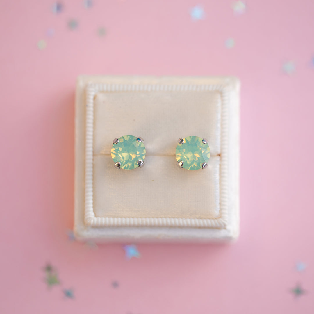 Pair of green gemstone stud earrings in a white box on a pink background