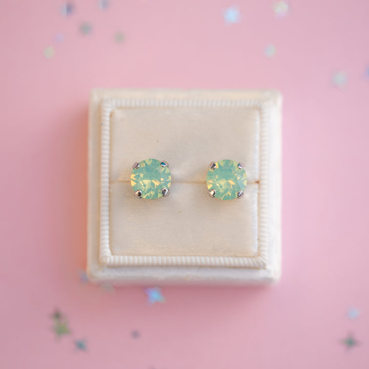 Pair of green gemstone stud earrings in a white box on a pink background