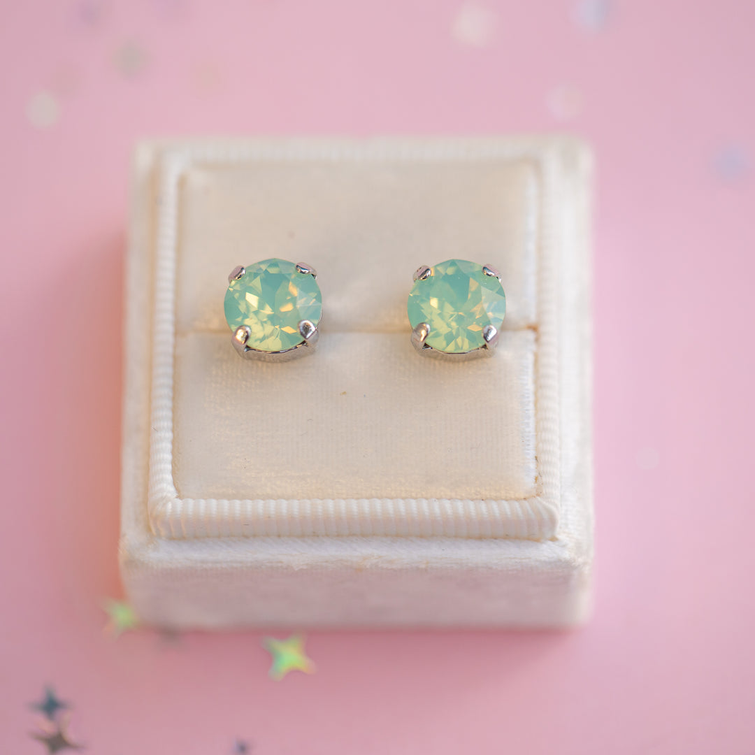 Pair of light blue opal stud earrings in a white box on a pink background