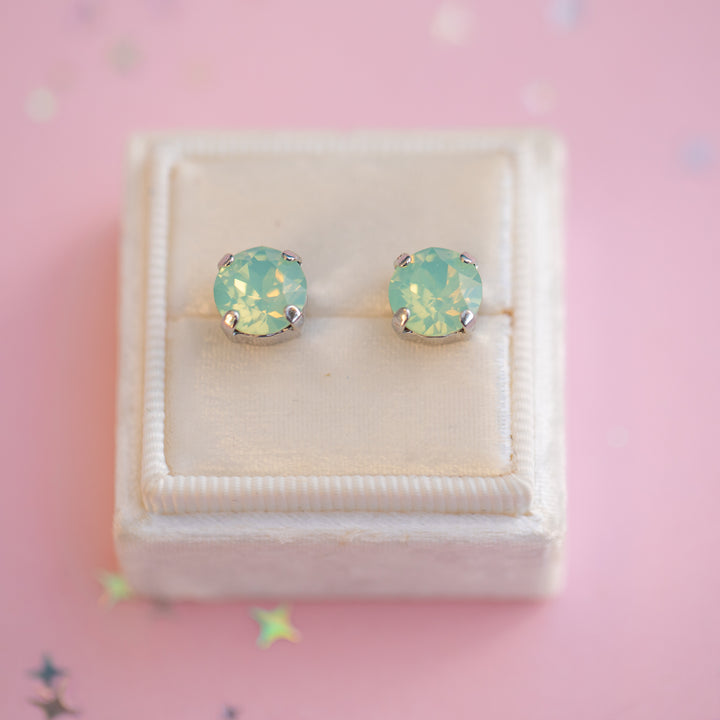 Pair of light blue opal stud earrings in a white box on a pink background