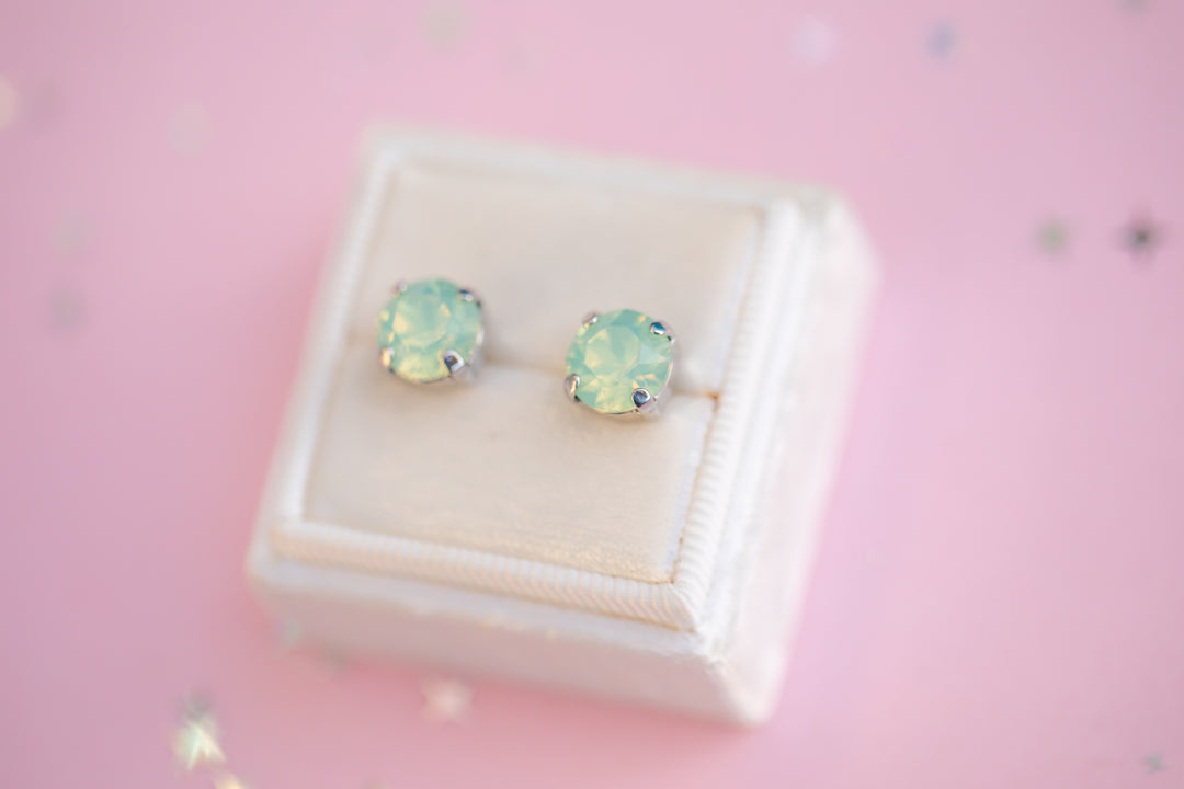 Pair of green gemstone stud earrings on a pink background
