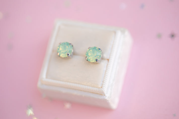 Pair of green gemstone stud earrings on a pink background