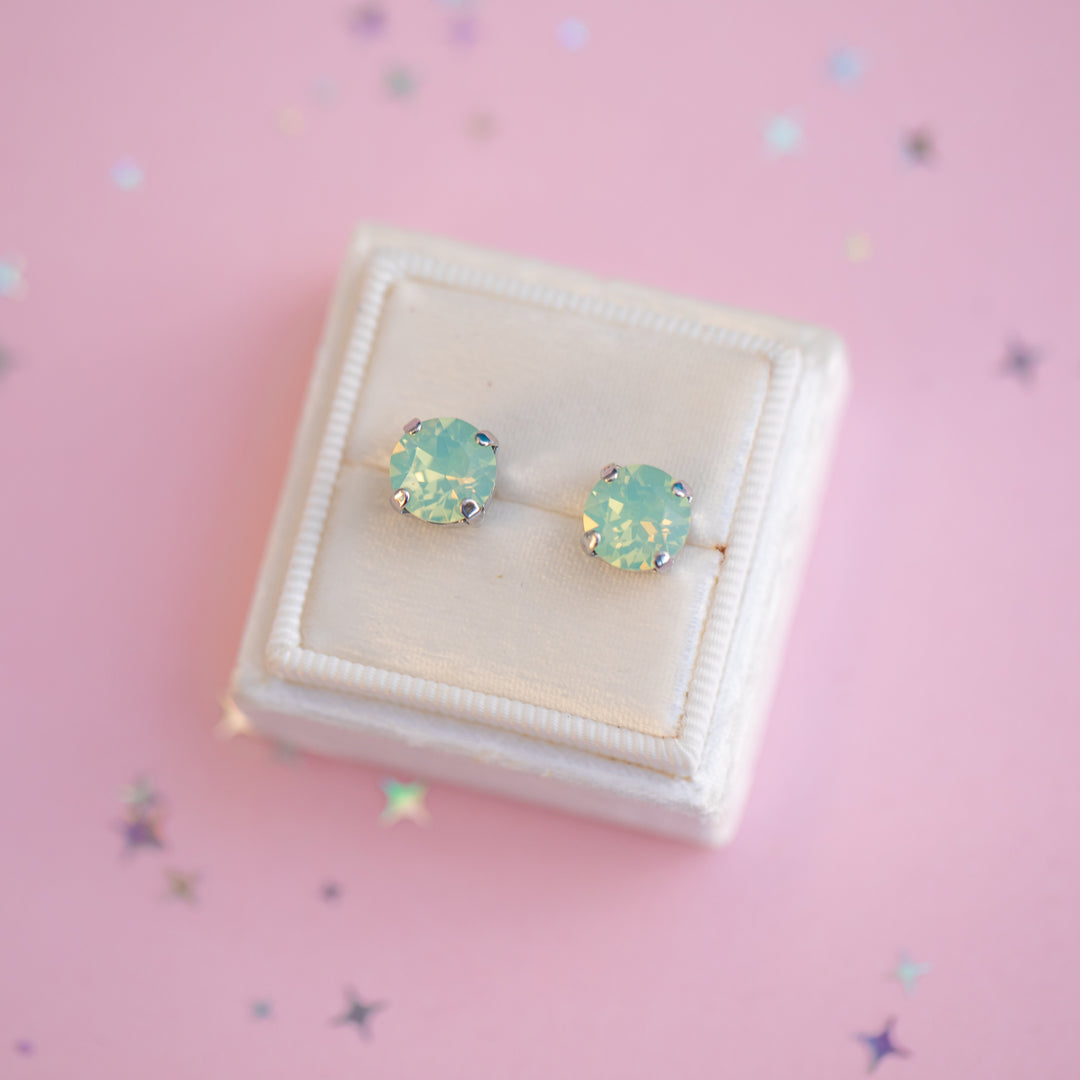 Pair of green gemstone earrings in a white jewelry box on a pink background