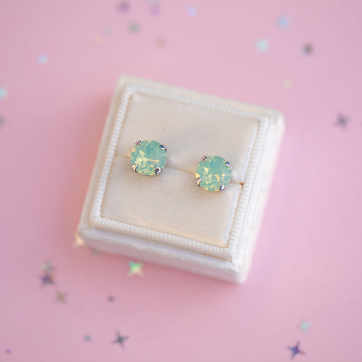 Pair of green gemstone earrings in a white jewelry box on a pink background