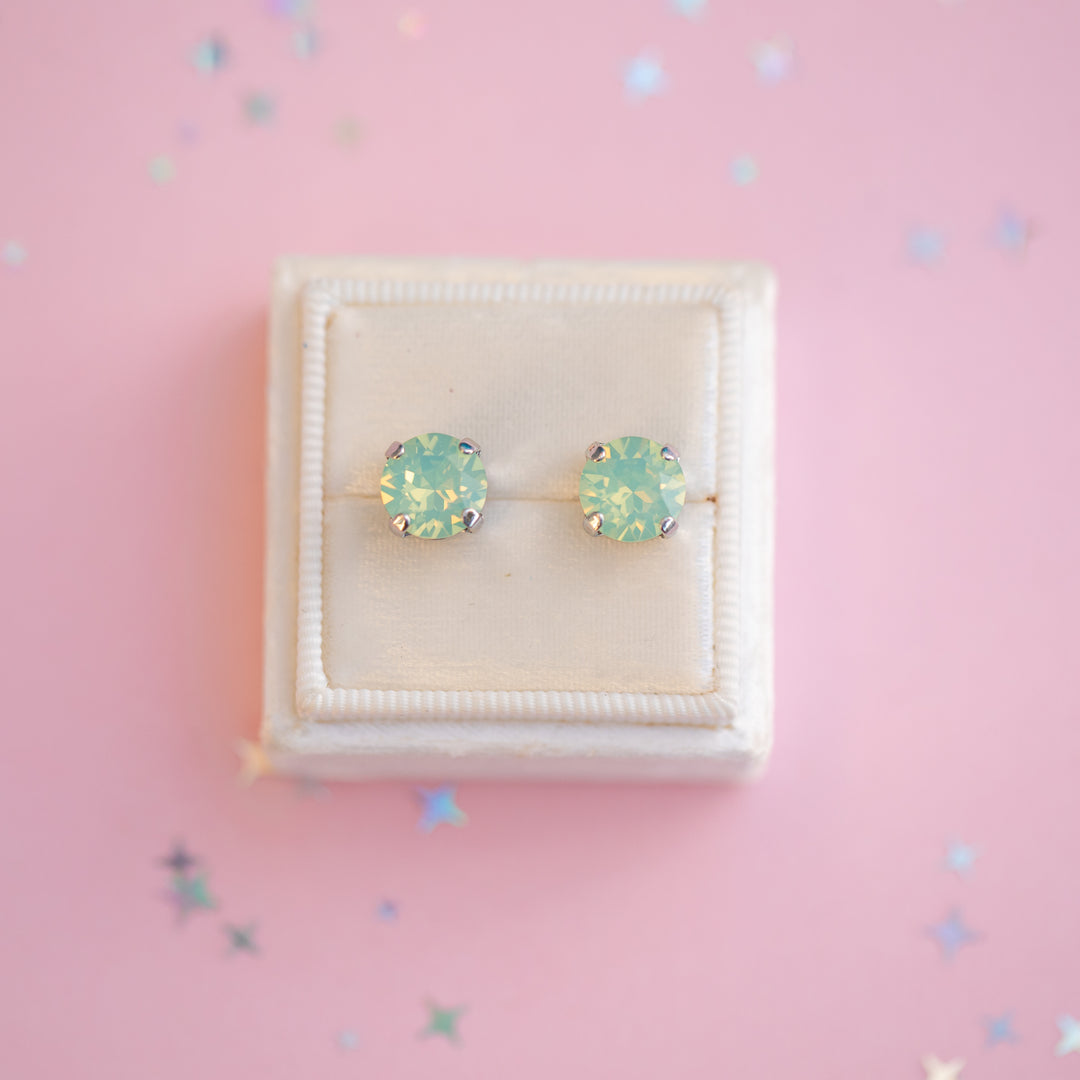 Pair of light blue stud earrings on a pink background