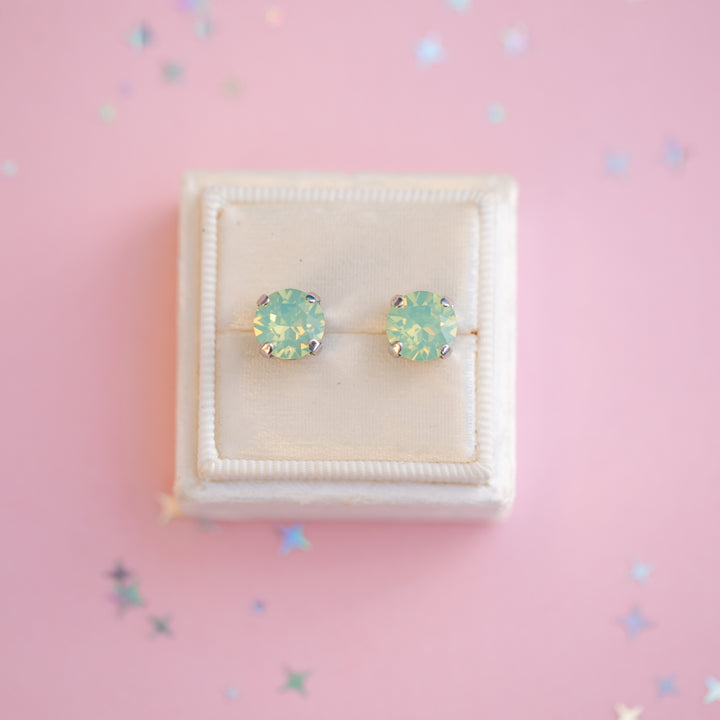 Pair of light blue stud earrings on a pink background