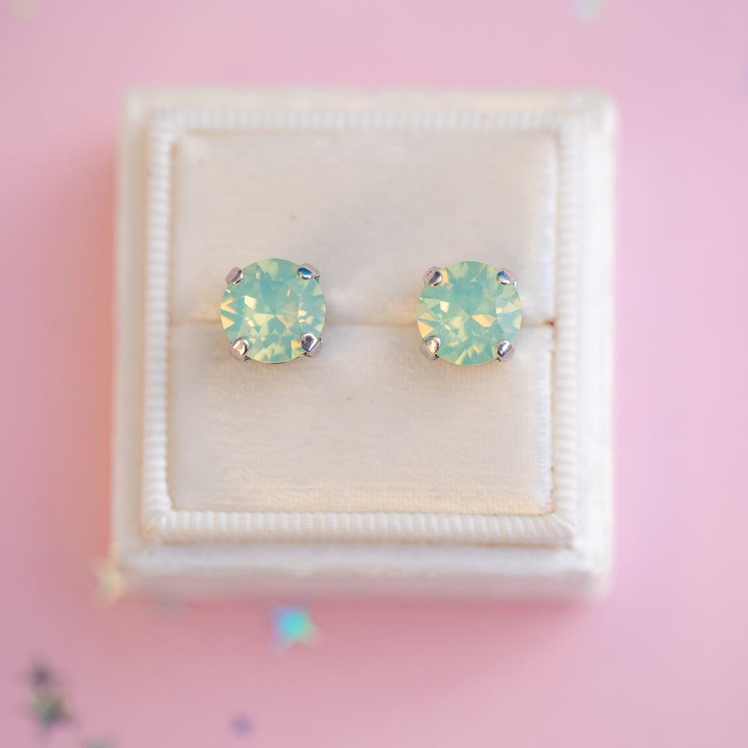 Pair of green opal stud earrings in a white box on a pink background