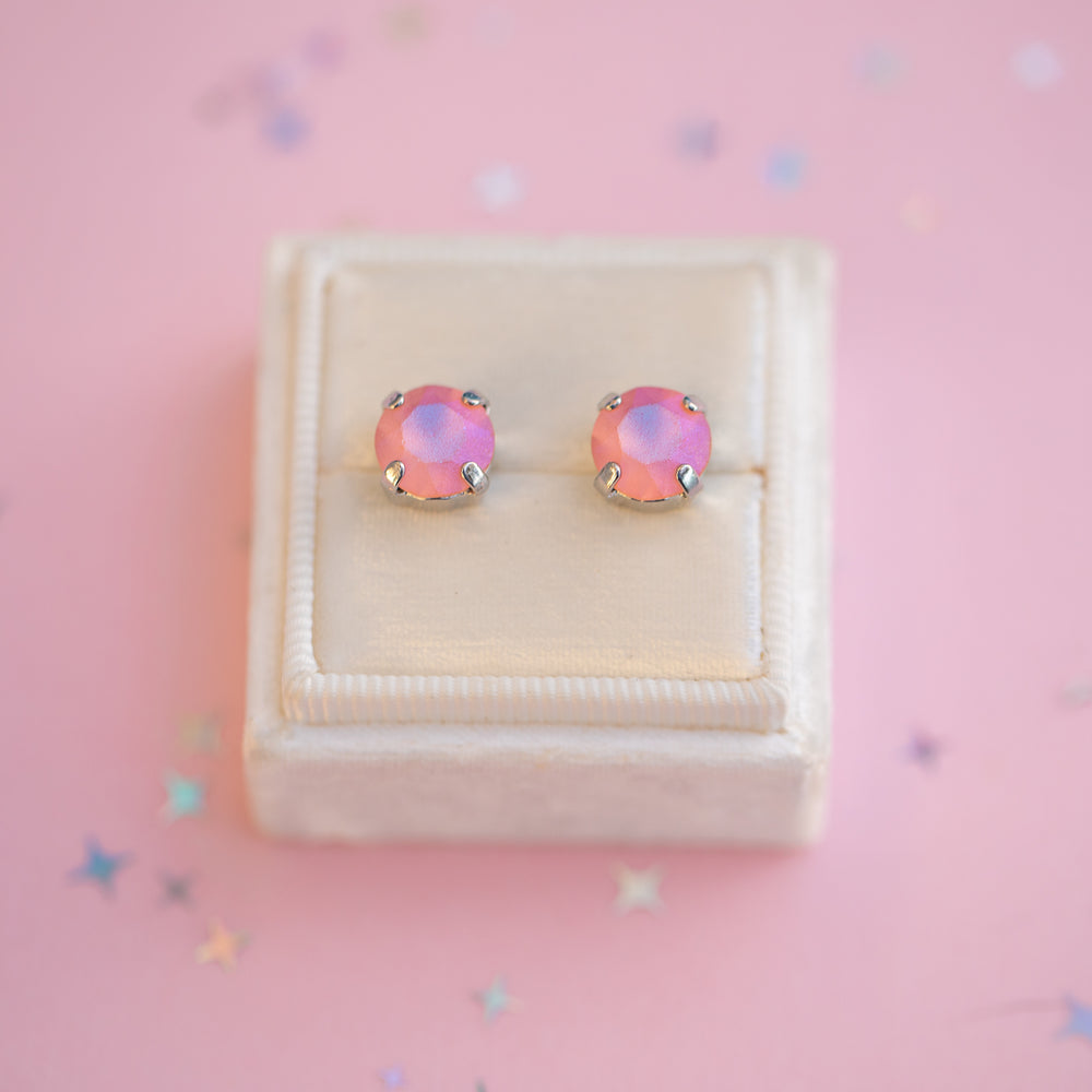 Pair of pink earrings in a white jewelry box on a pink background with star-shaped decorations.