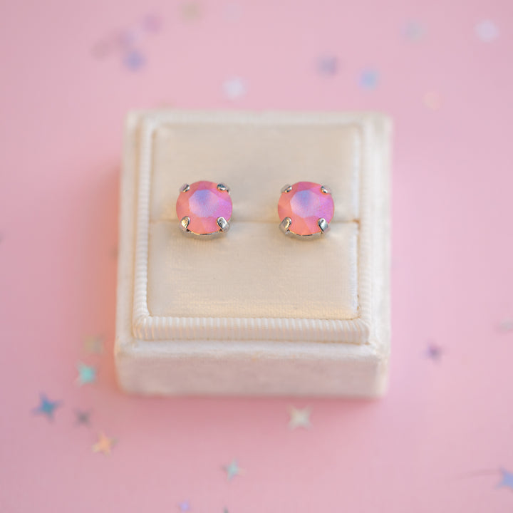 Pair of pink earrings in a white jewelry box on a pink background with star-shaped decorations.