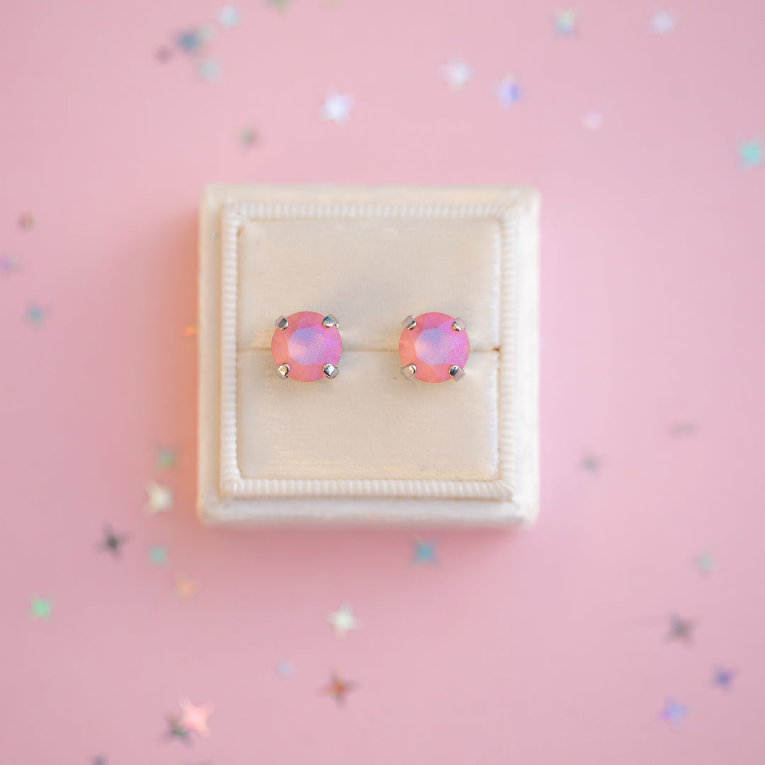 Pair of pink earrings in a white box on a pink background with confetti.