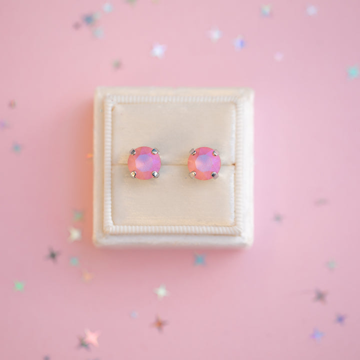 Pair of pink earrings in a white box on a pink background with confetti.