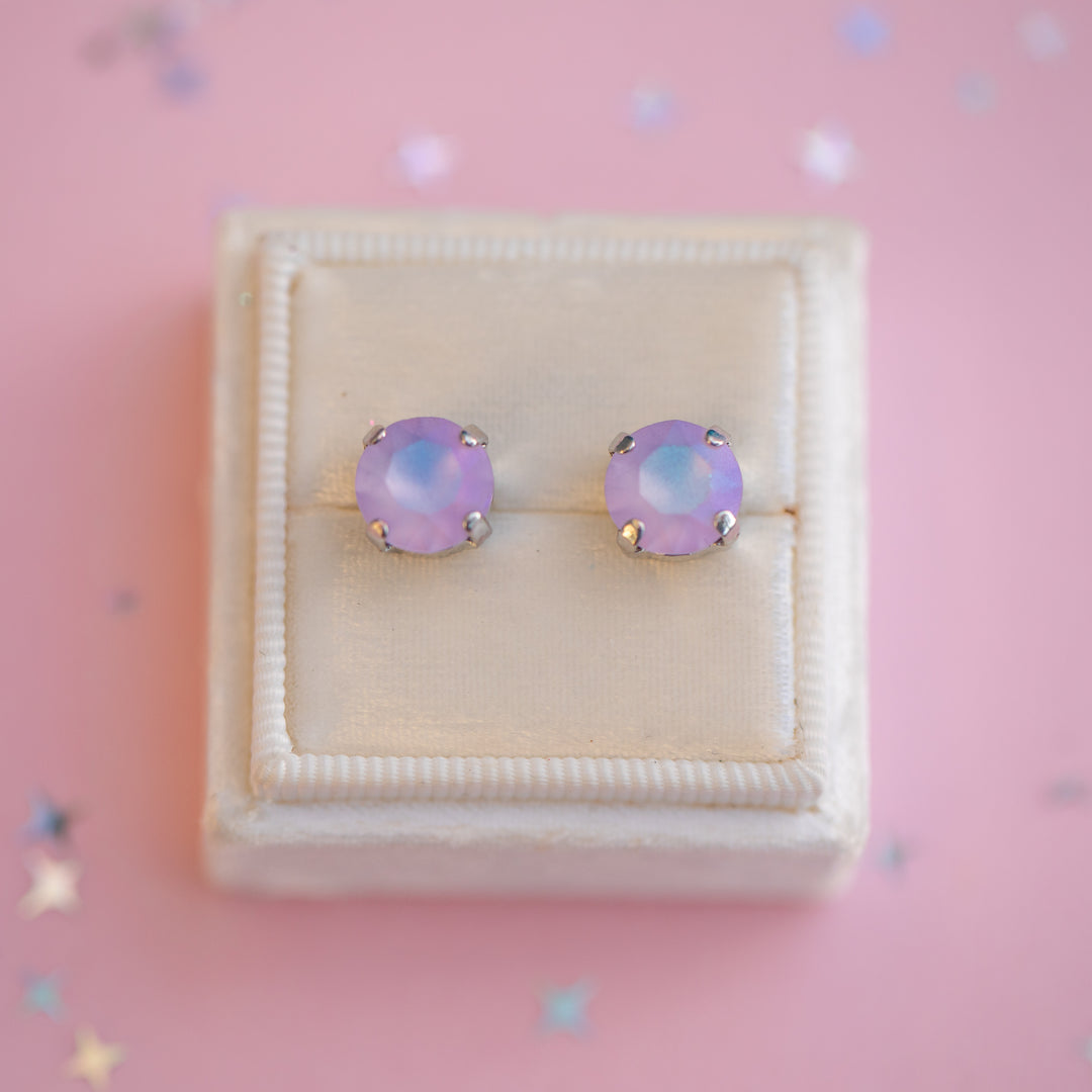 Pair of purple stud earrings in a jewelry box on a pink background with star decorations.
