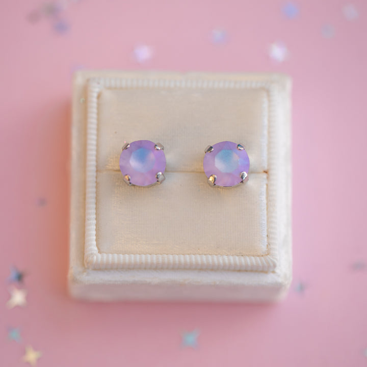 Pair of purple stud earrings in a jewelry box on a pink background with star decorations.