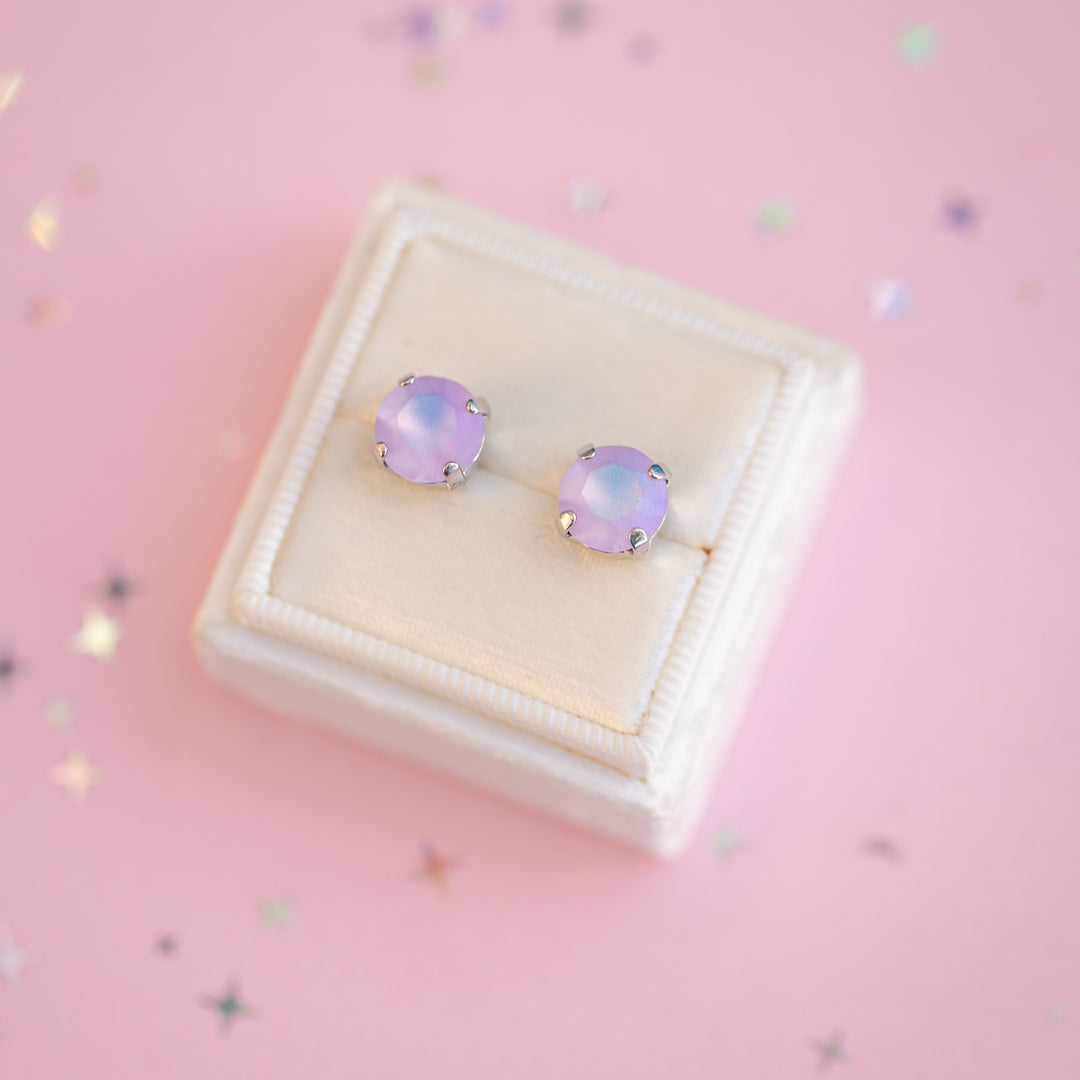 Pair of purple gemstone earrings in a white jewelry box on a pink background