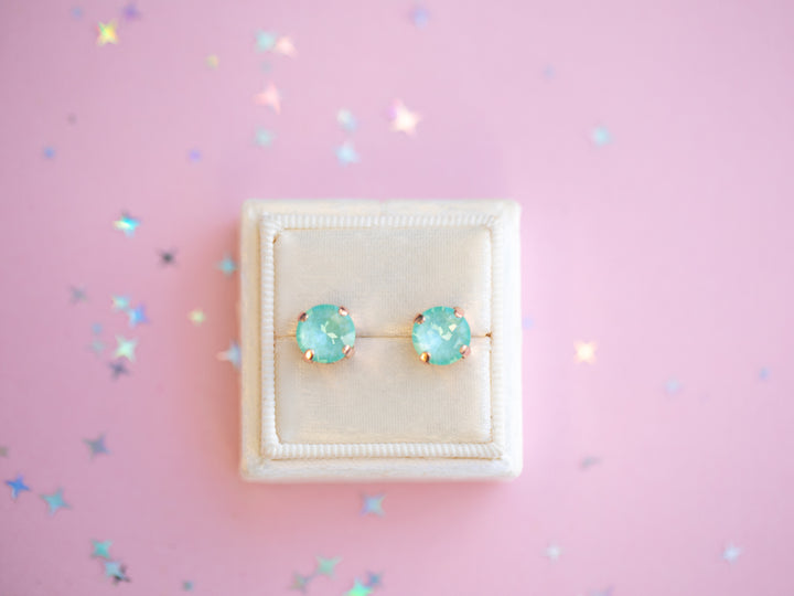 Pair of turquoise stud earrings in a white box on a pink background with confetti.