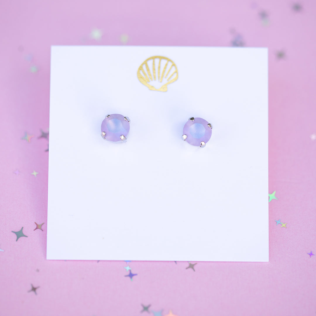 Pair of purple round earrings on a white card with a gold shell logo on a pink background.