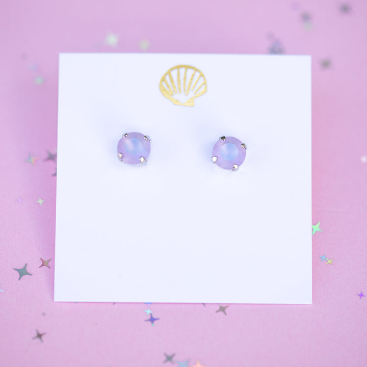 Pair of purple round earrings on a white card with a gold shell logo on a pink background.