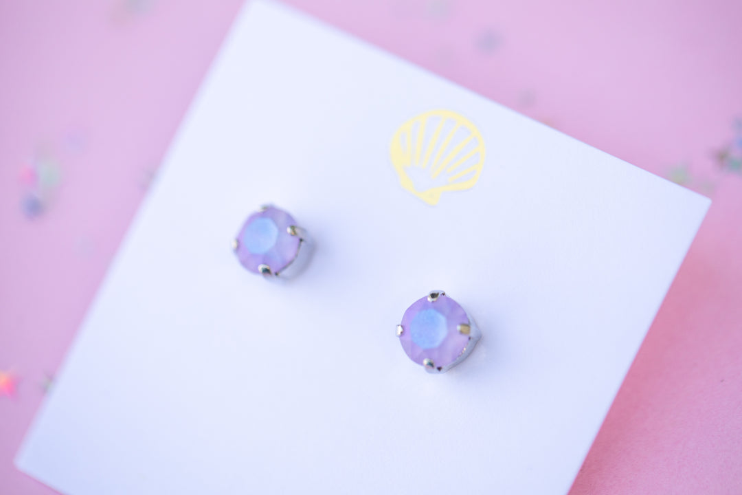 purple stud earrings on a white card with a logo against a pink background
