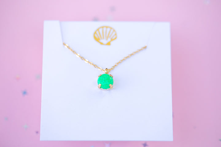 Gold necklace with a green pendant on a white card against a pink background