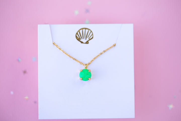 Gold necklace with a green pendant on a white card against a pink background