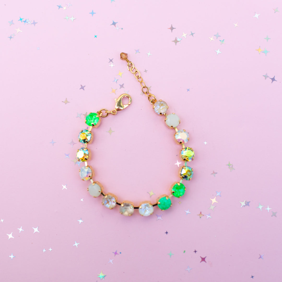 Gold bracelet with colorful gemstones on a pink background with star-shaped confetti