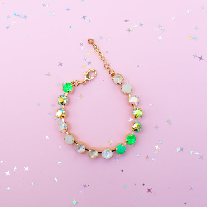 Gold bracelet with colorful gemstones on a pink background with star-shaped confetti