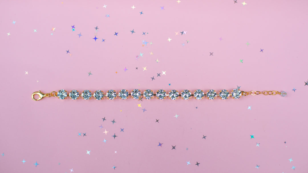 Gold bracelet with blue gemstones on a pink background with star-shaped glitter