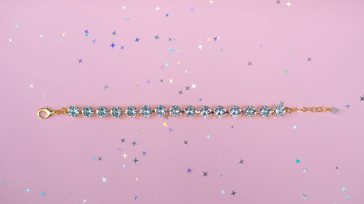 Gold bracelet with blue gemstones on a pink background with star-shaped glitter
