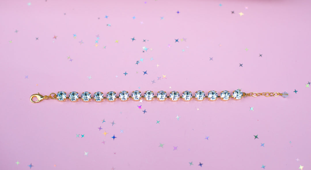 Gold bracelet with blue crystals on a pink background