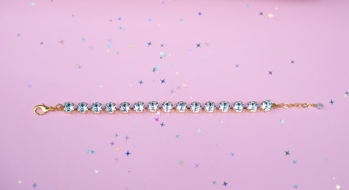 Gold bracelet with blue crystals on a pink background