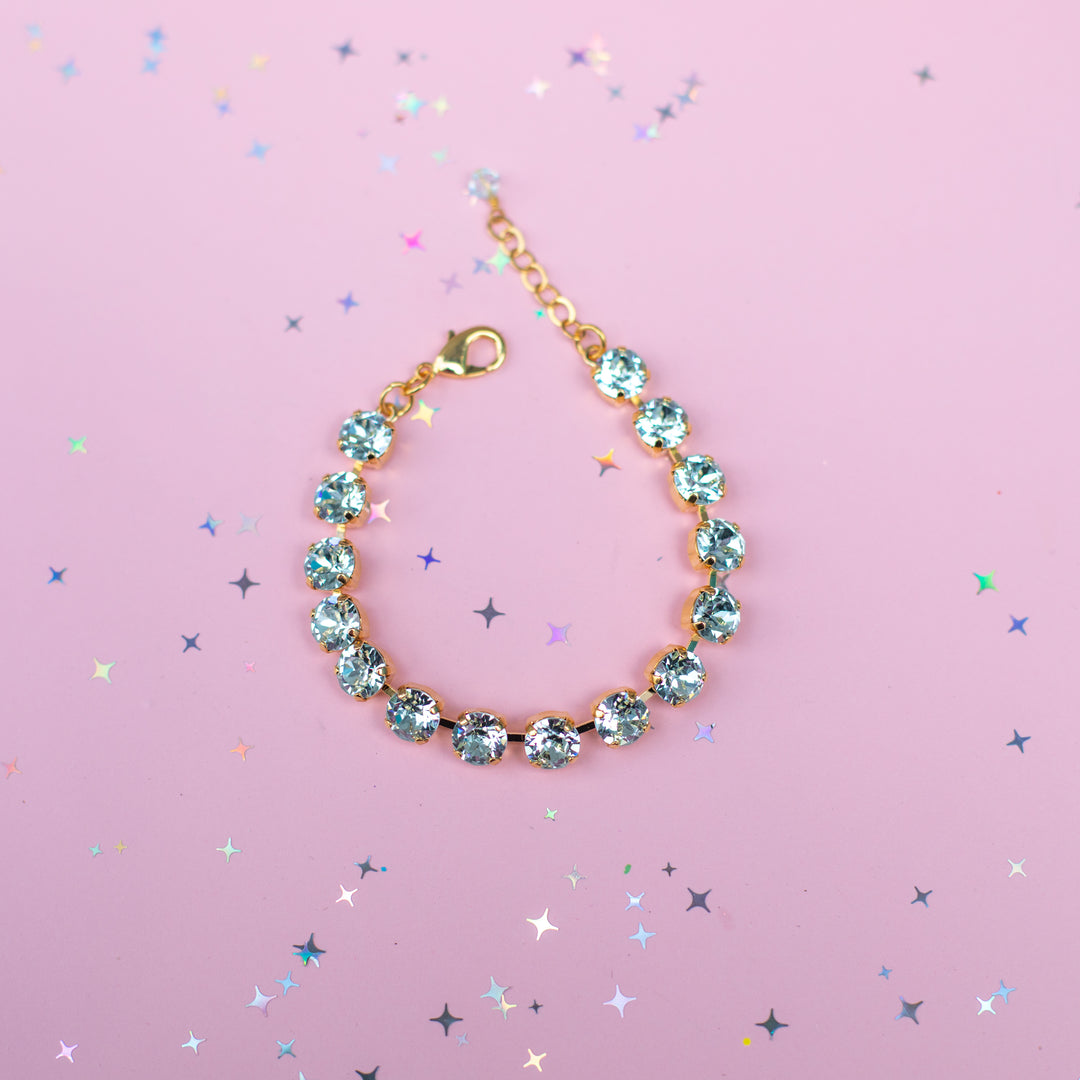 Gold bracelet with blue gemstones on a pink background with star-shaped confetti