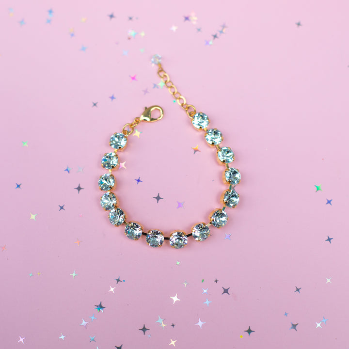 Gold bracelet with blue gemstones on a pink background with star-shaped confetti