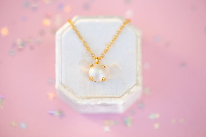 Pearl necklace with gold chain in a hexagonal white box on a pink background