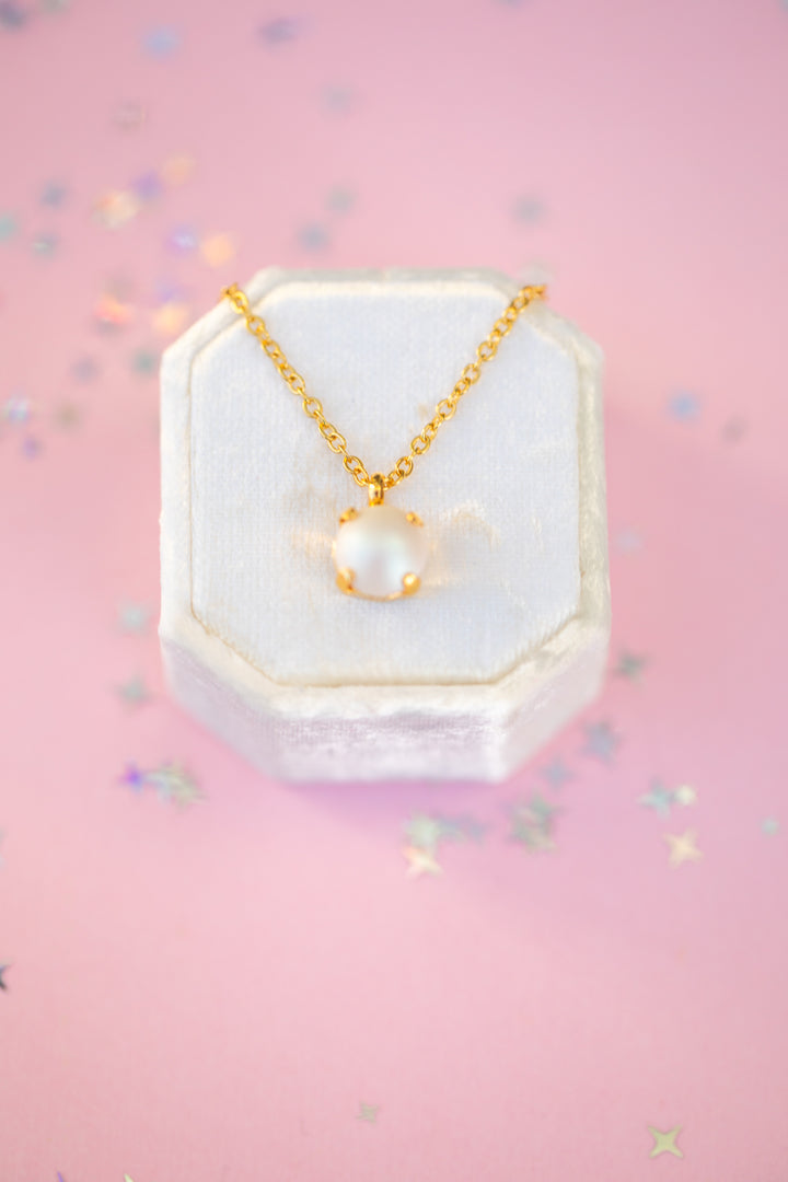 Gold necklace with a pearl pendant on a pink background