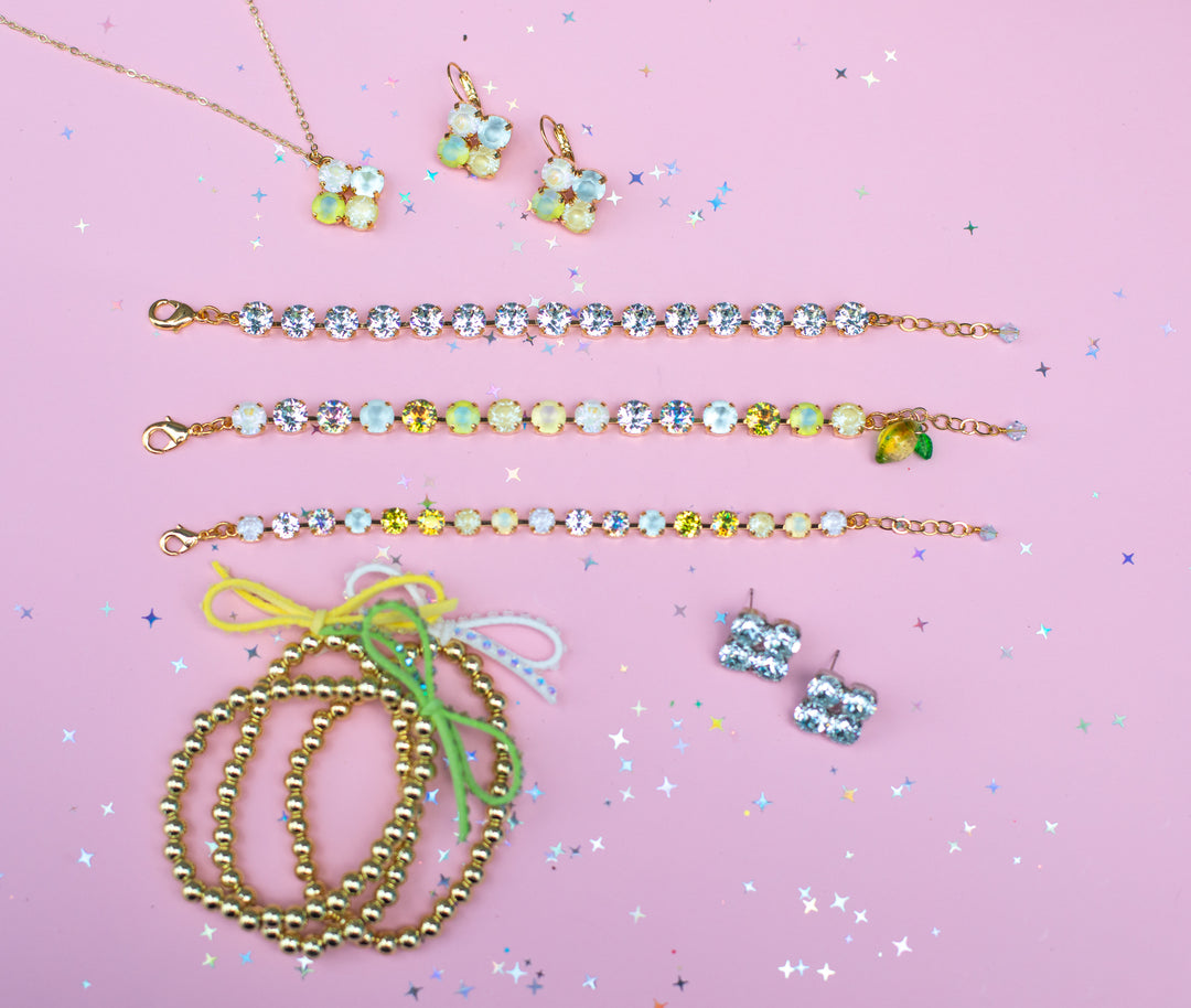 Jewelry set including necklaces, bracelets, and earrings on a pink background with confetti.