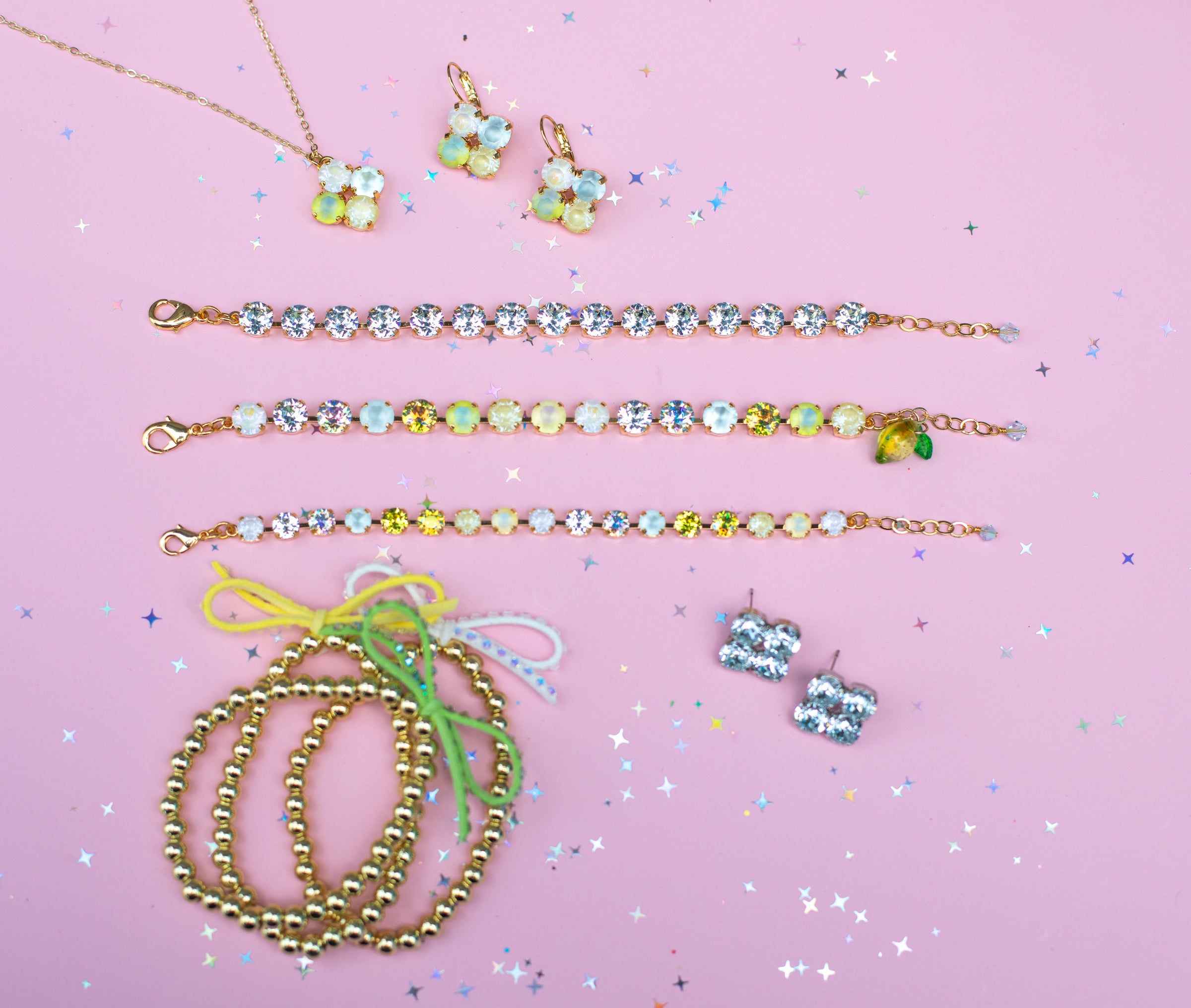 Jewelry set including necklaces, bracelets, and earrings on a pink background with confetti.