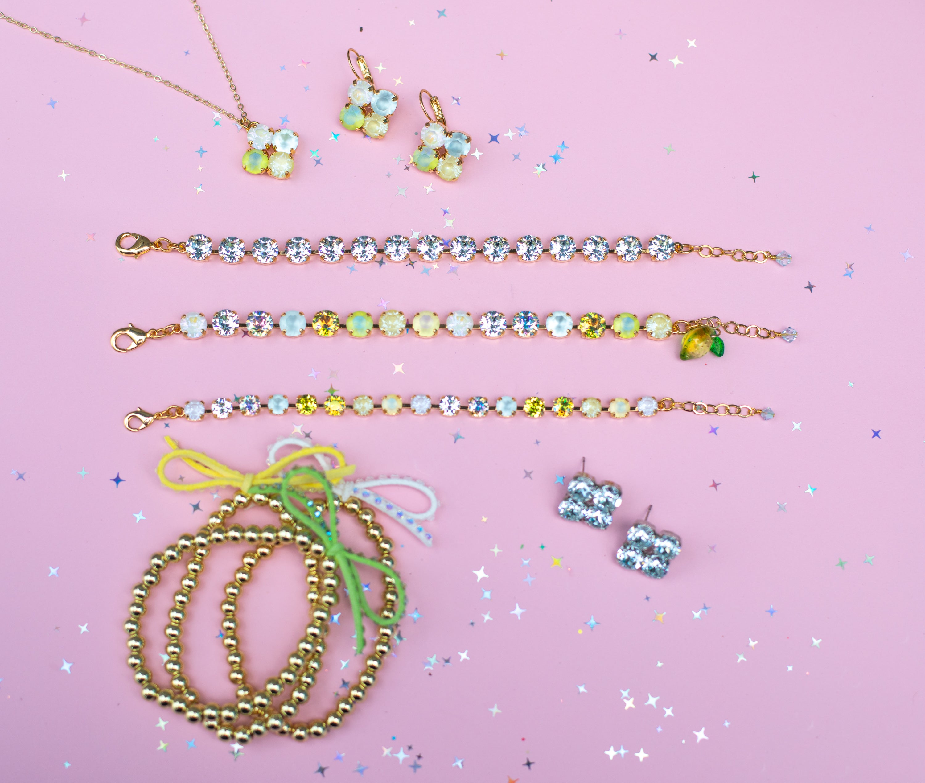 Jewelry set including necklaces, bracelets, and earrings on a pink background with confetti.