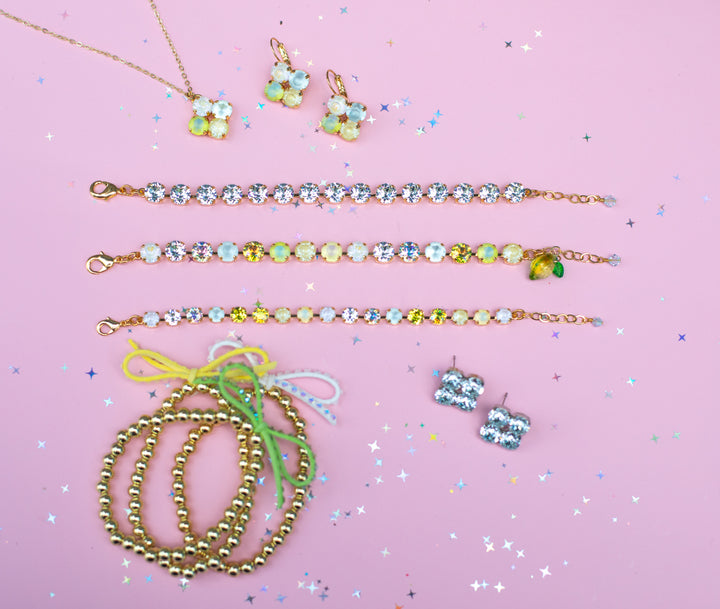 Jewelry set including necklaces, bracelets, and earrings on a pink background with confetti.