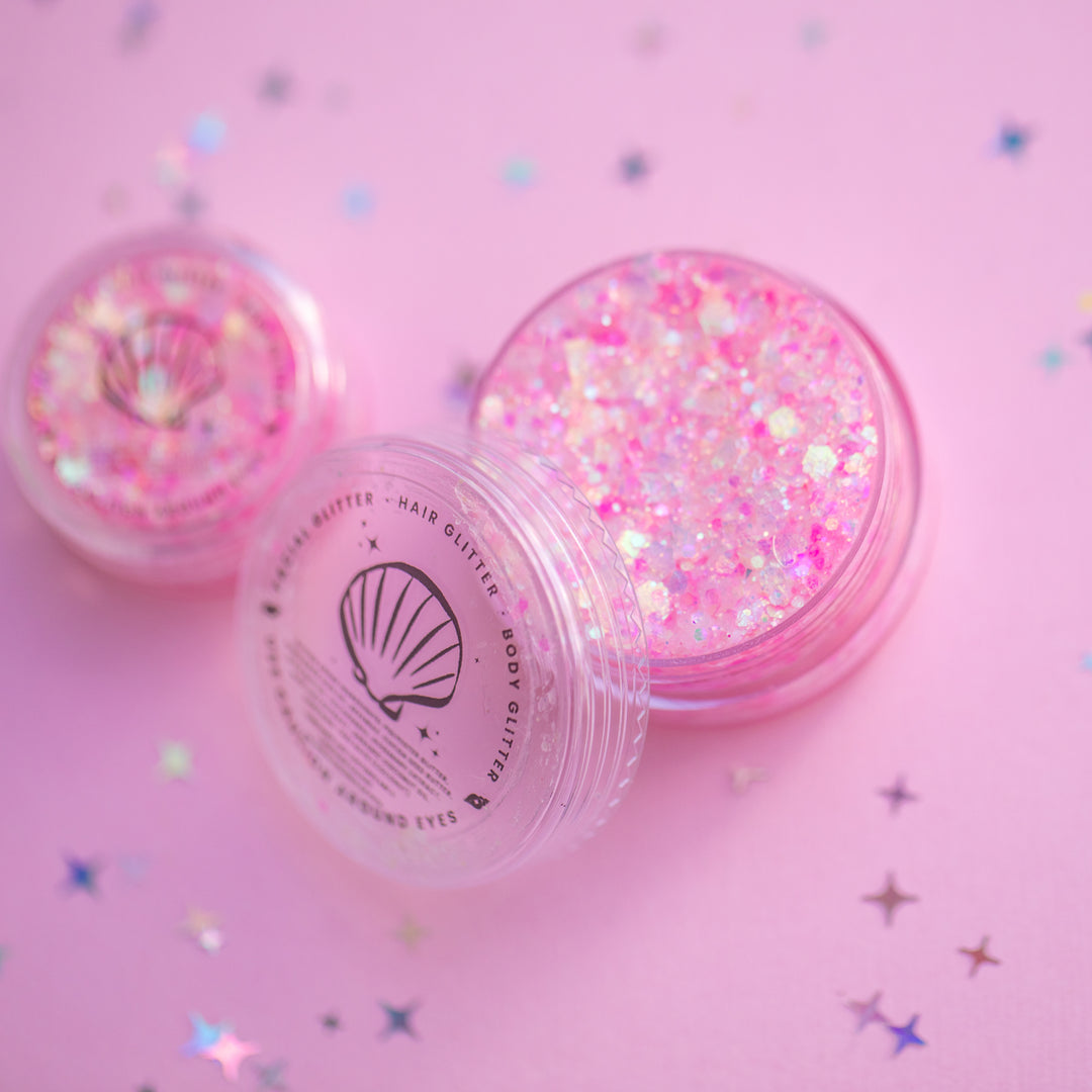 Two containers of pink glitter on a pink background with star-shaped confetti.